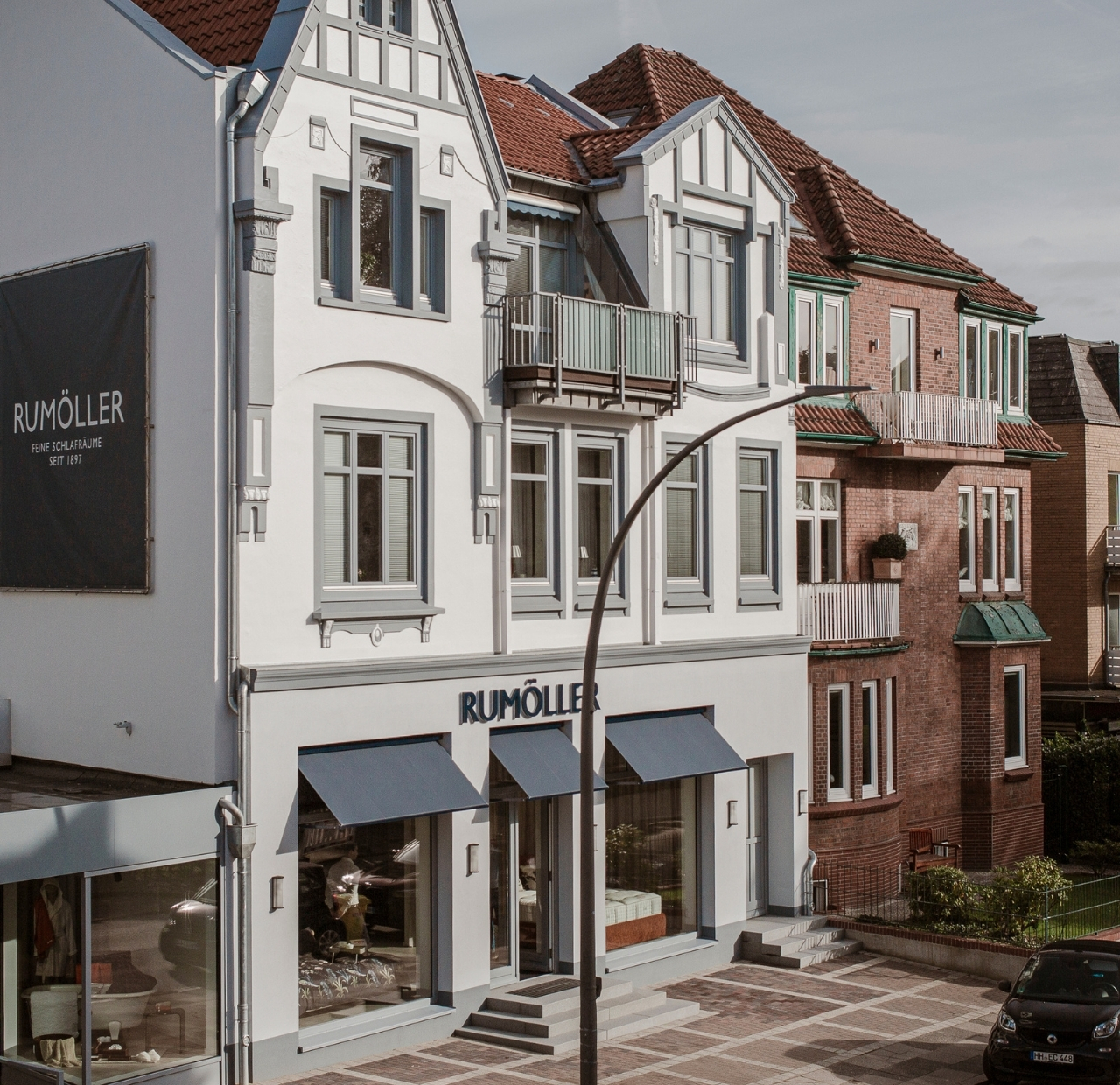 Geschäftsfassade, Weiße Fassade, Backsteinfassade, Rotes Ziegeldach, Graue Markisen, 