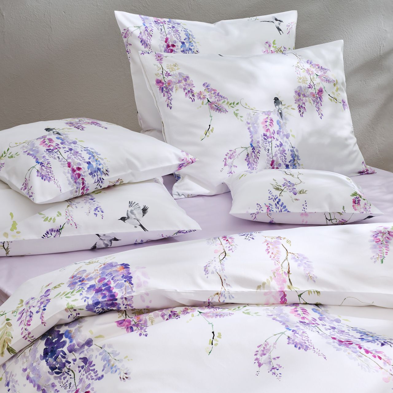 Mehrere Kissen auf einem Bett mit lila Blumenmuster