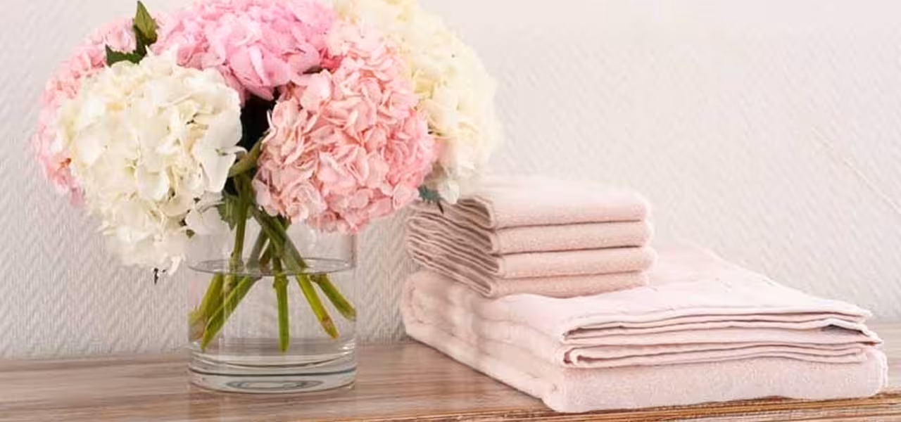Handtuchstapel in rosa auf Holzplatte neben rosa Blumenstrauß
