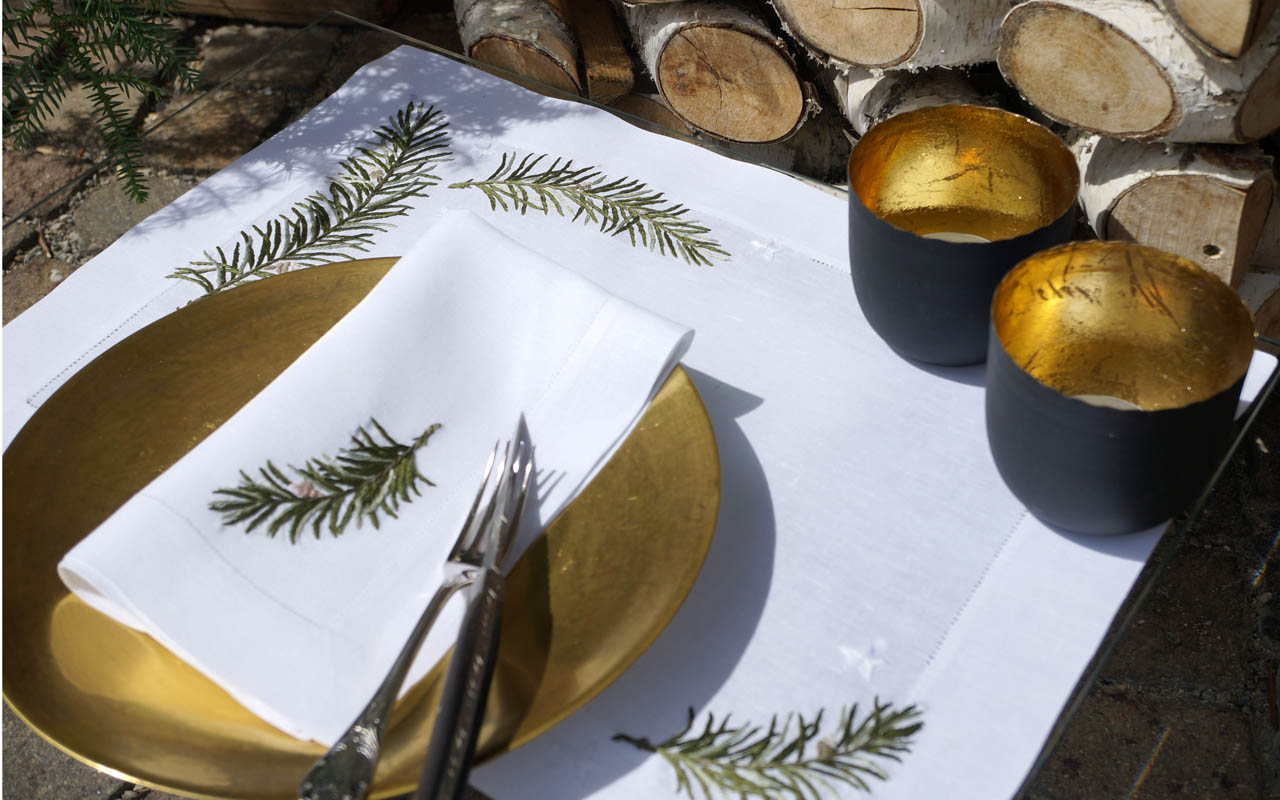 Handbestickte Leinen Tischdecke von Eri Goldener Teller auf weißer Leinen Tischdecke und Serviette mit gesticktem Rosmarinmotiv