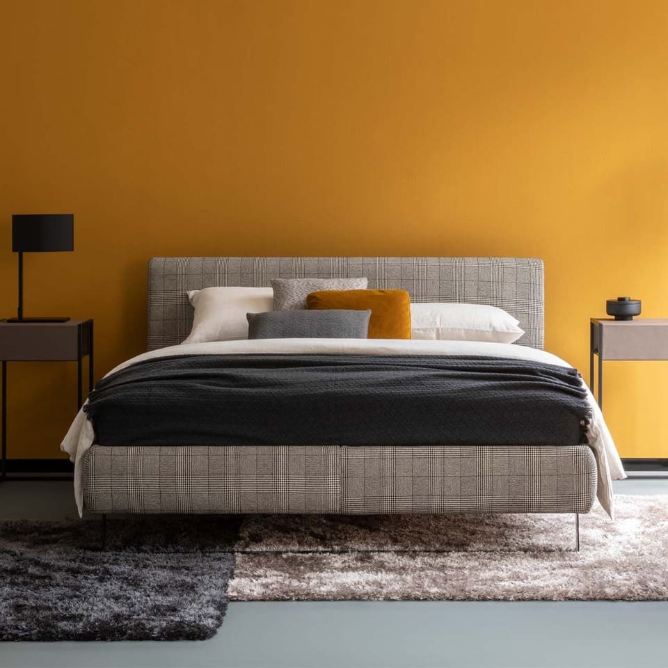 Christine Kröncke Schlafzimmermöbel Bett und Nachttische von Christine Kröncke in Grautönen vor senfgelber Wand