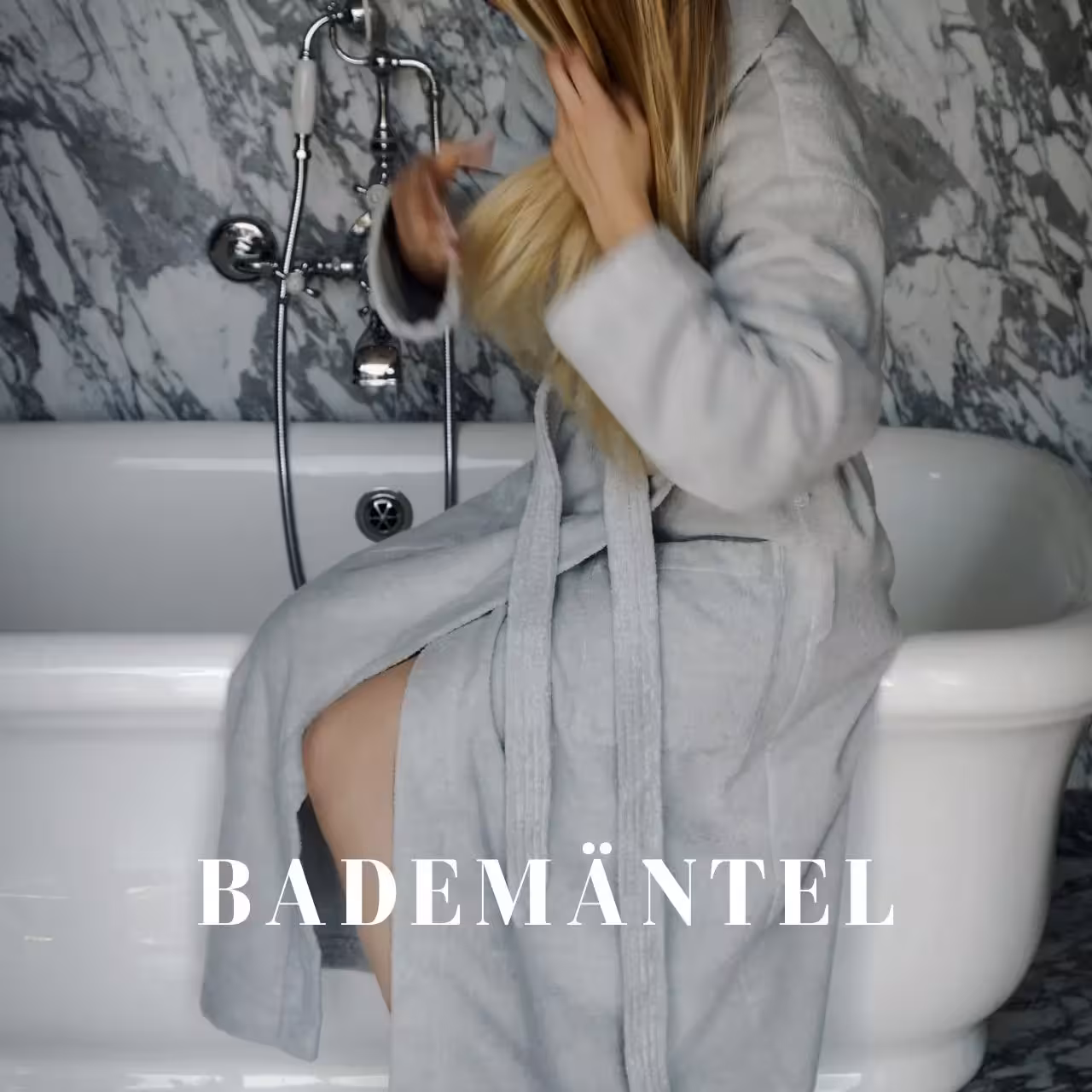 Frau in grauem Bademantel sitzt auf Badewannenrand