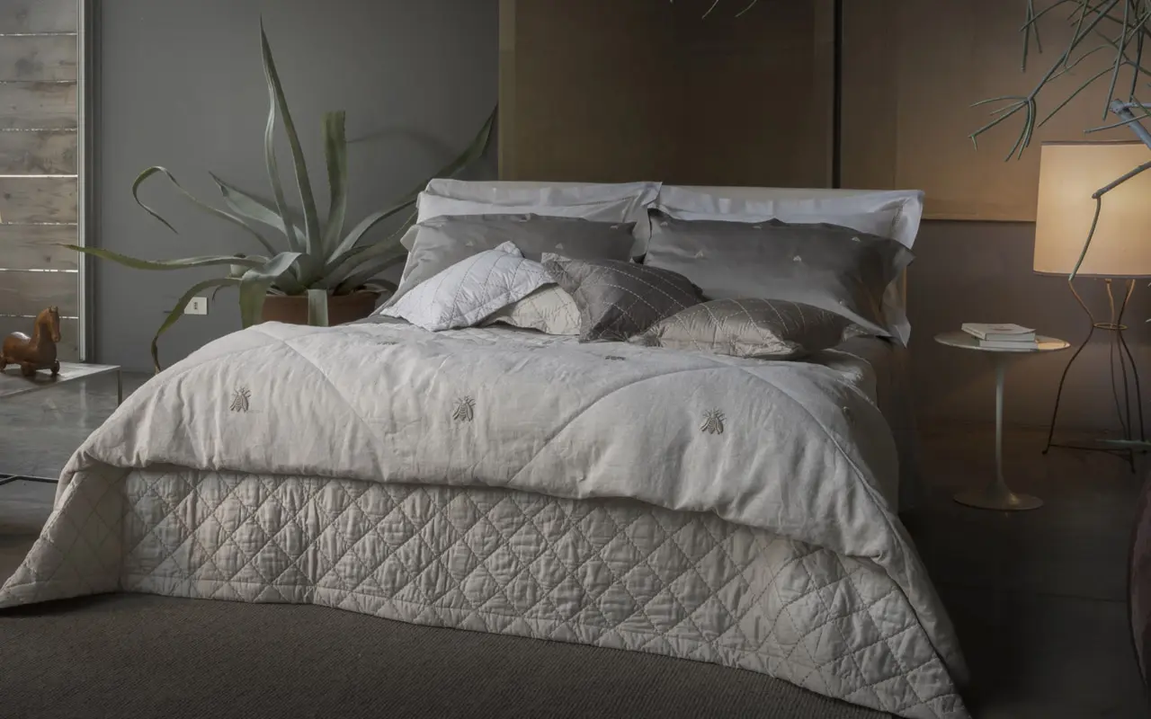 Elegantes Bett mit Tagesdecke neben großer Grünpflanze