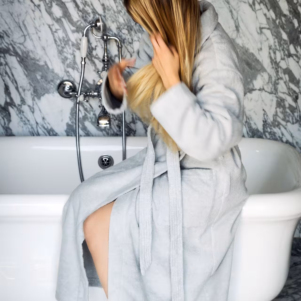 Frau in Bademantel auf Badewannenrand